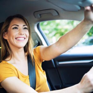 Happy woman adjusting rearview mirror while driving.