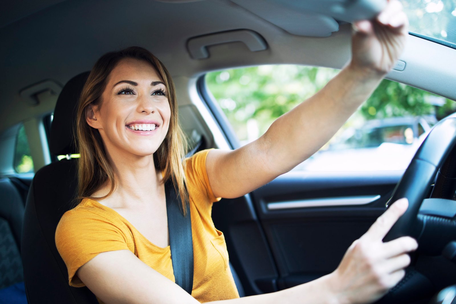 Happy woman adjusting rearview mirror while driving.